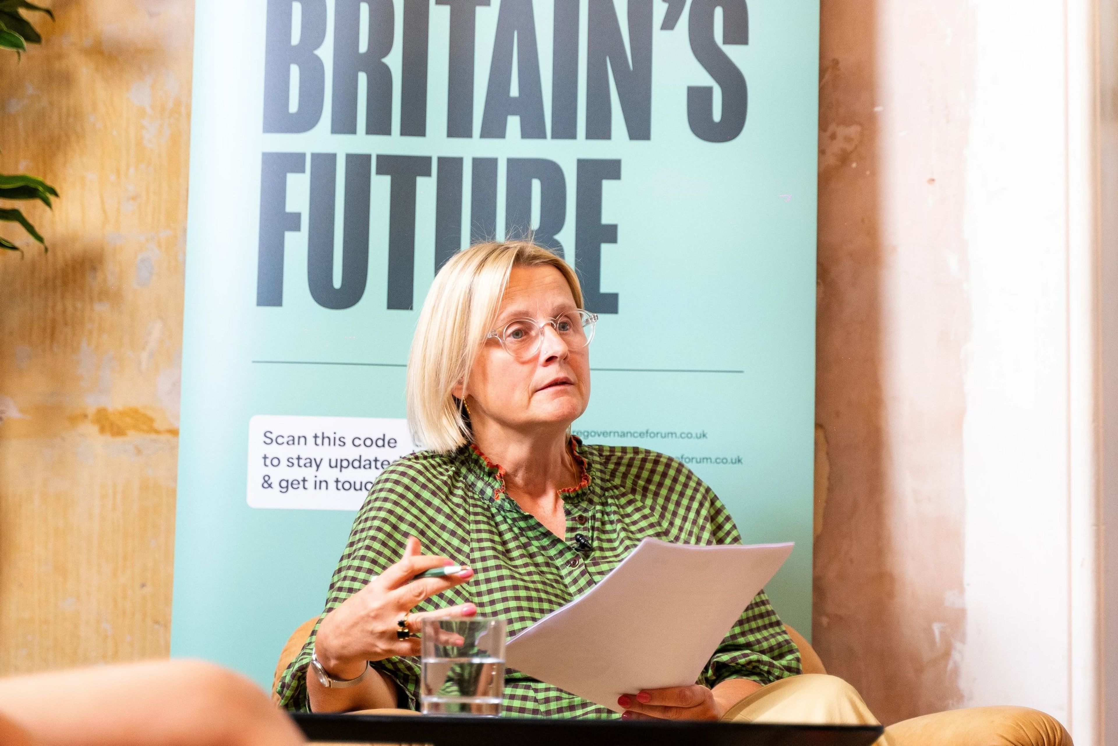 A woman is sitting on a chair while delivering a talk next to a banner that reads "Britain's future"