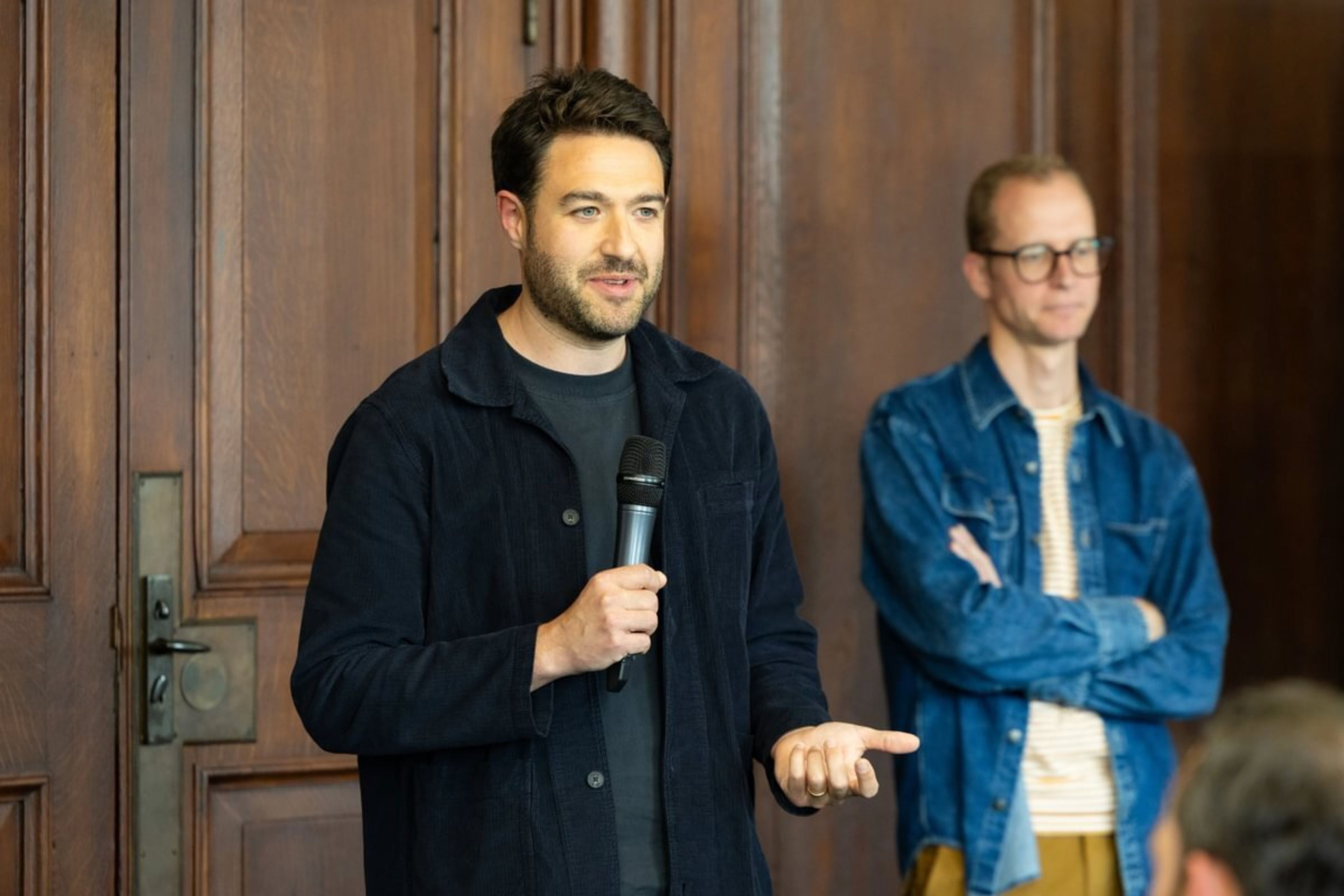 A man with a microphone is delivering a talk next to another speaker