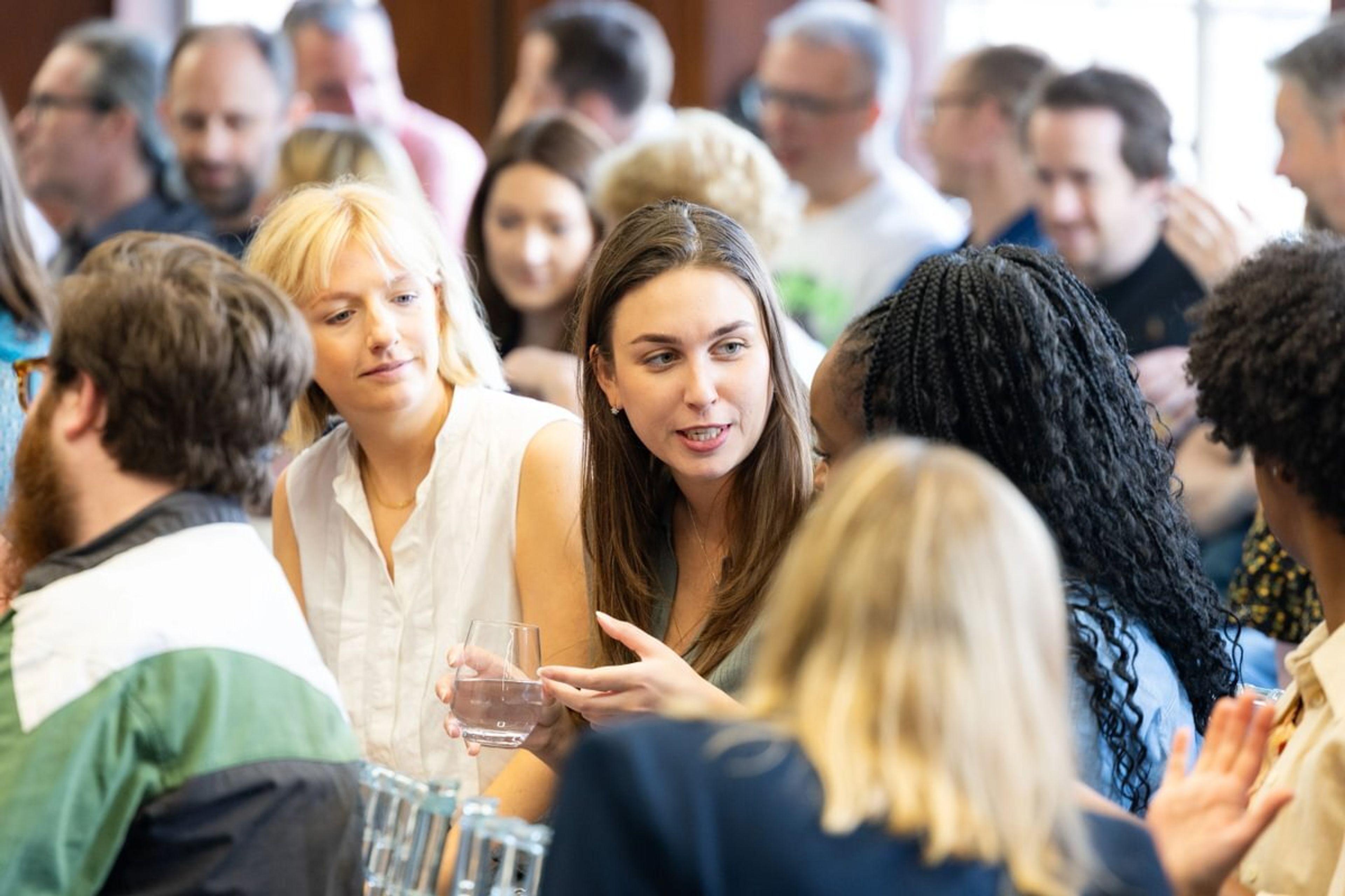 A woman is sat surrounded by people as part of the audience of an event