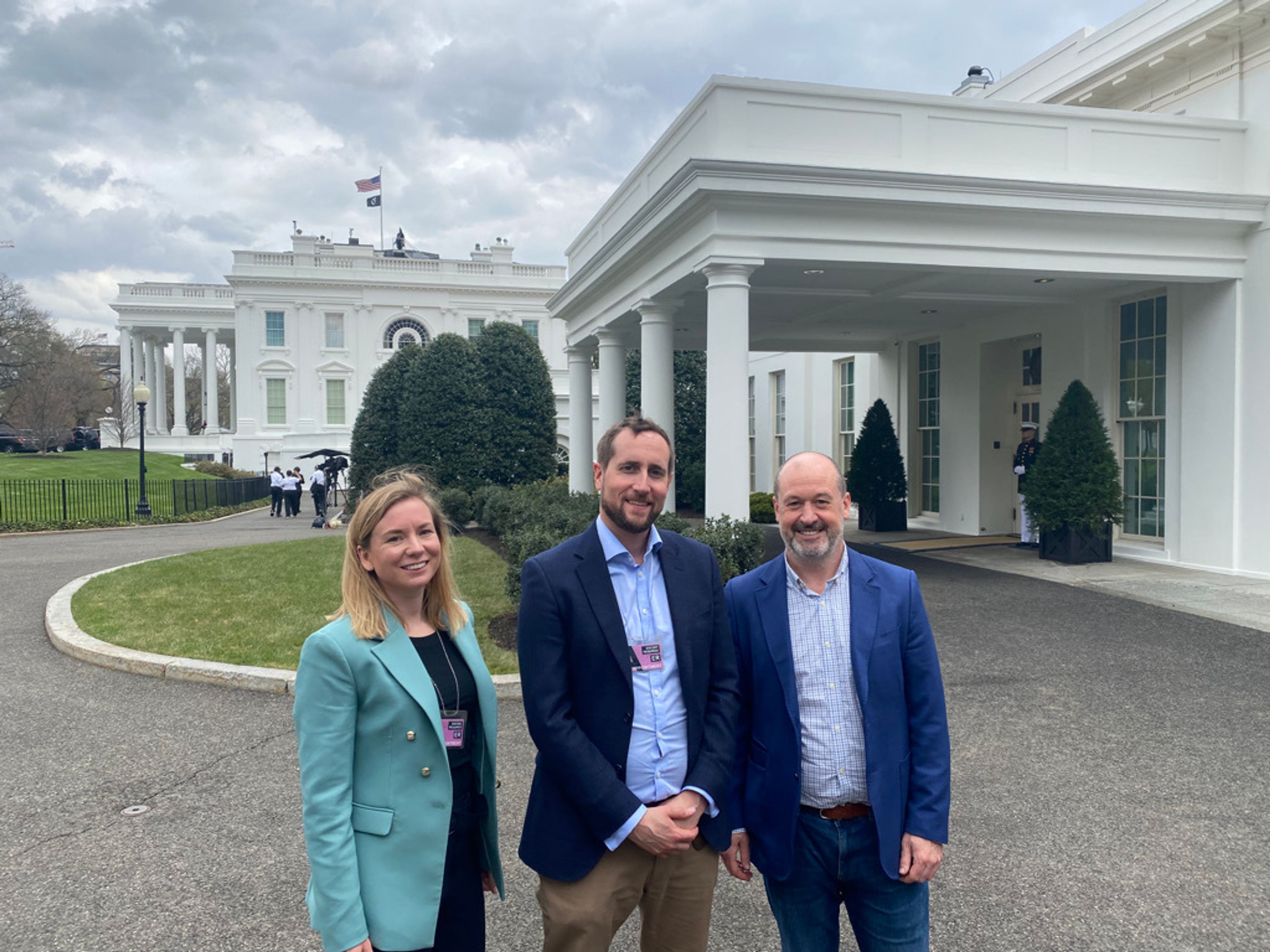 Three people pose to camera next to the White House