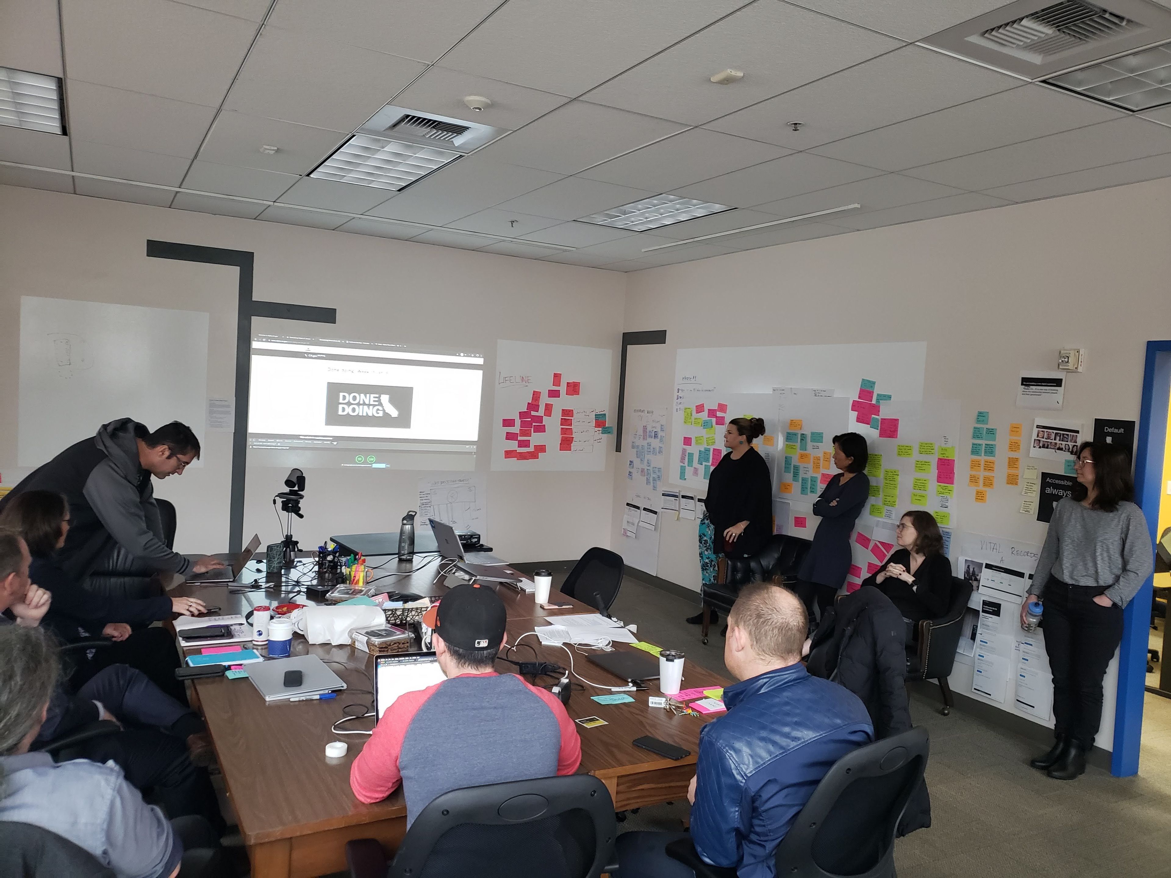 A group of people working across a busy room with screens and paper artifacts on the walls