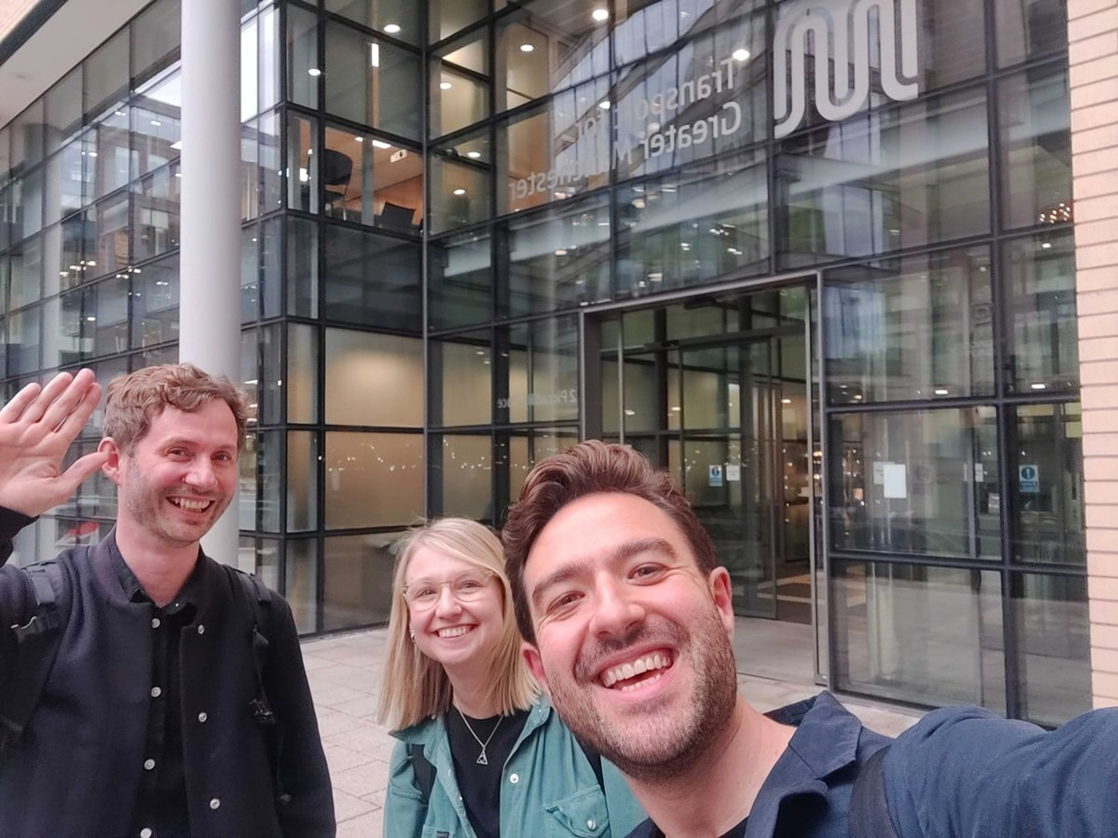 Three people smiling and taking a selfie in front of a building