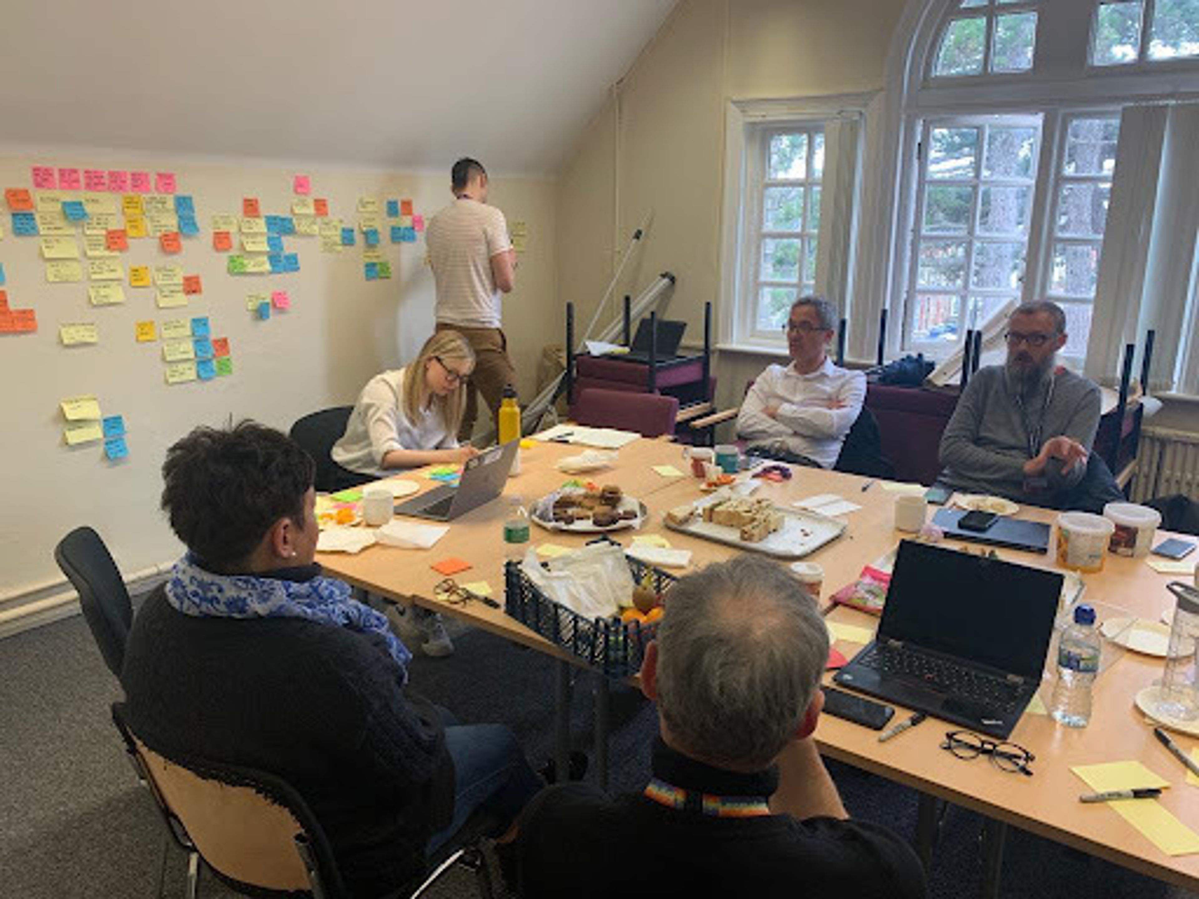 A group of people sitting in a room working collaboratively while another member takes notes on a wall