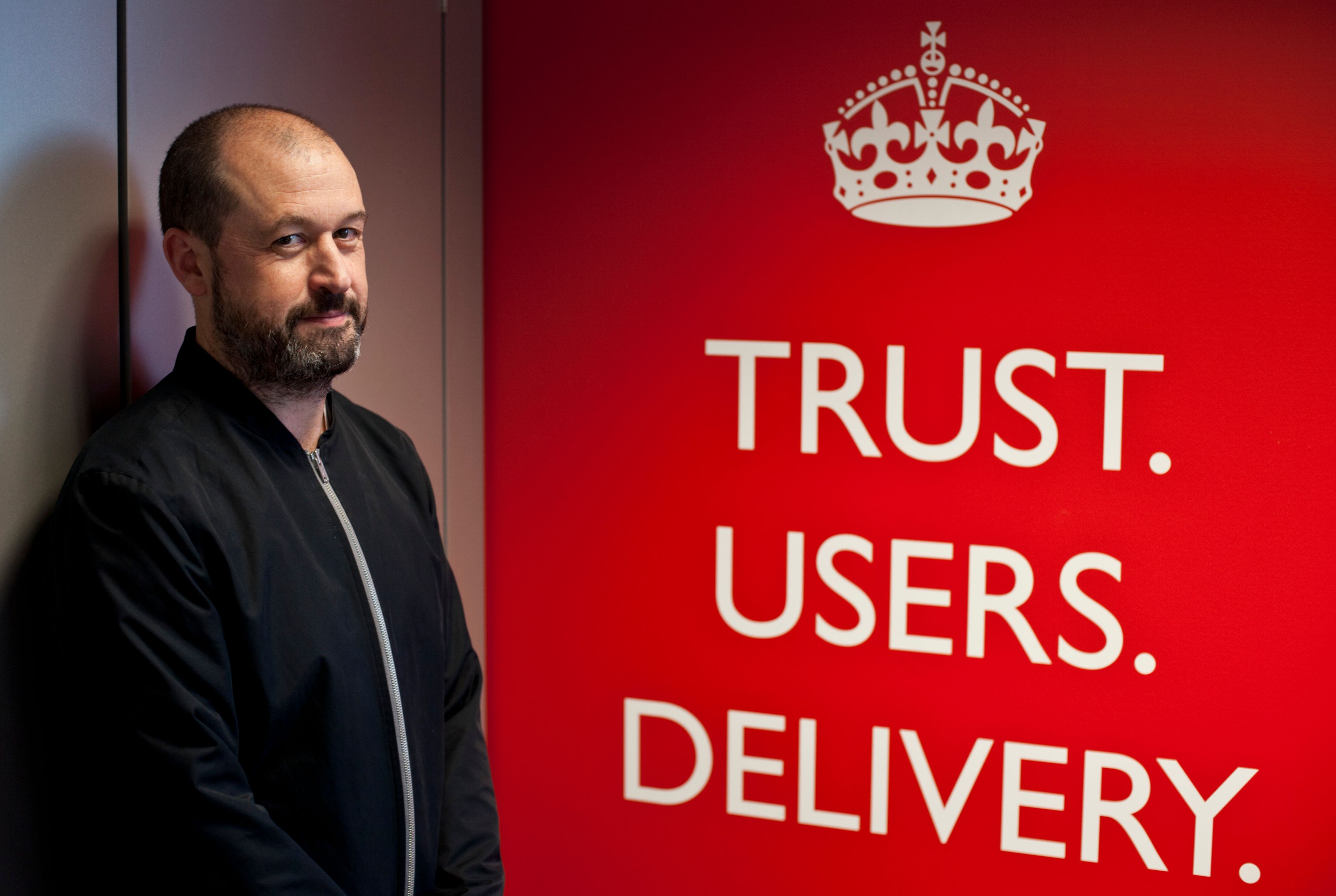Mike Bracken in front of a poster that reads: Trust. Users. Delivery