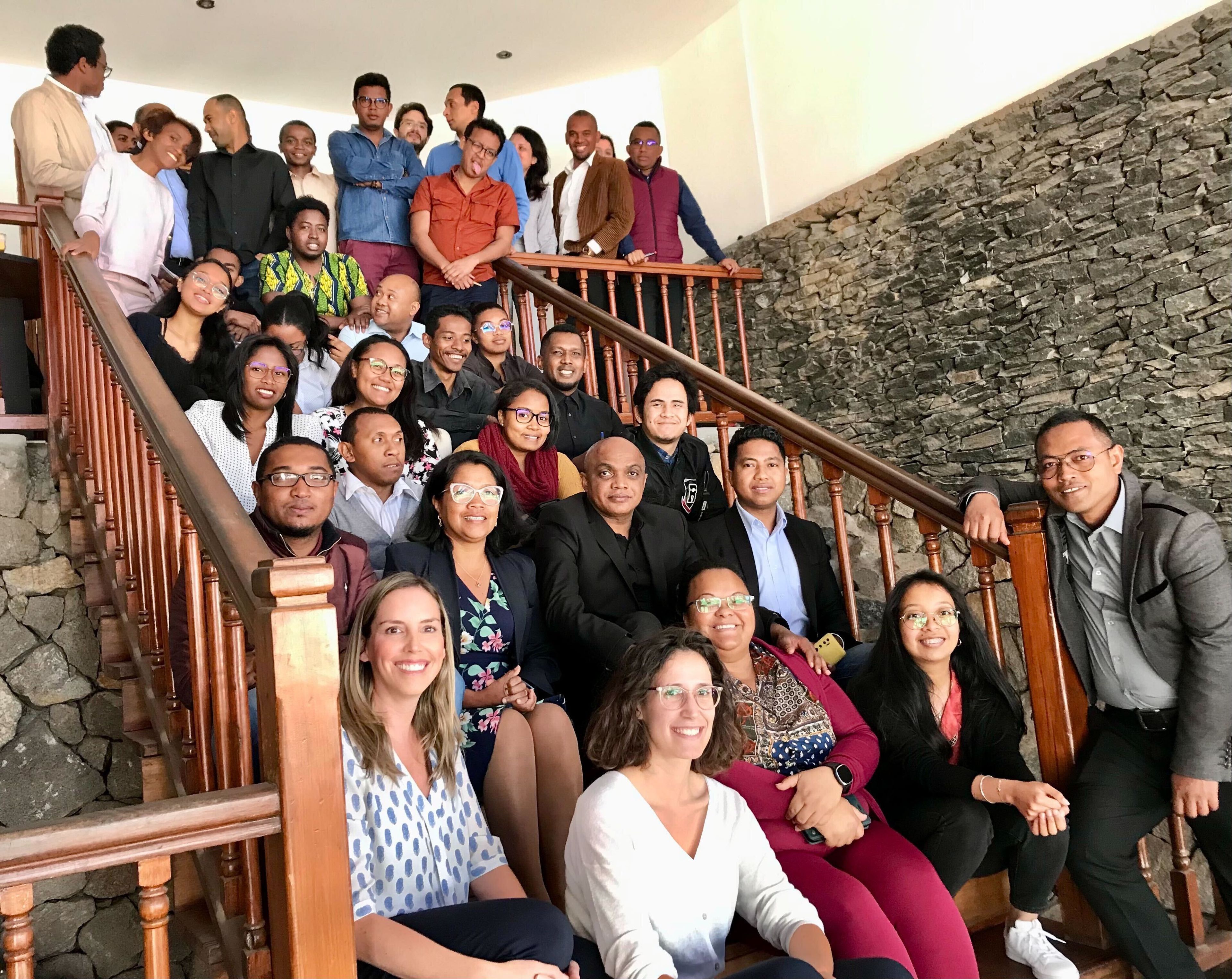 A large group of people all siting across a staircase with some looking at camera and smiling and others talking amongst themselves with a jovial tone