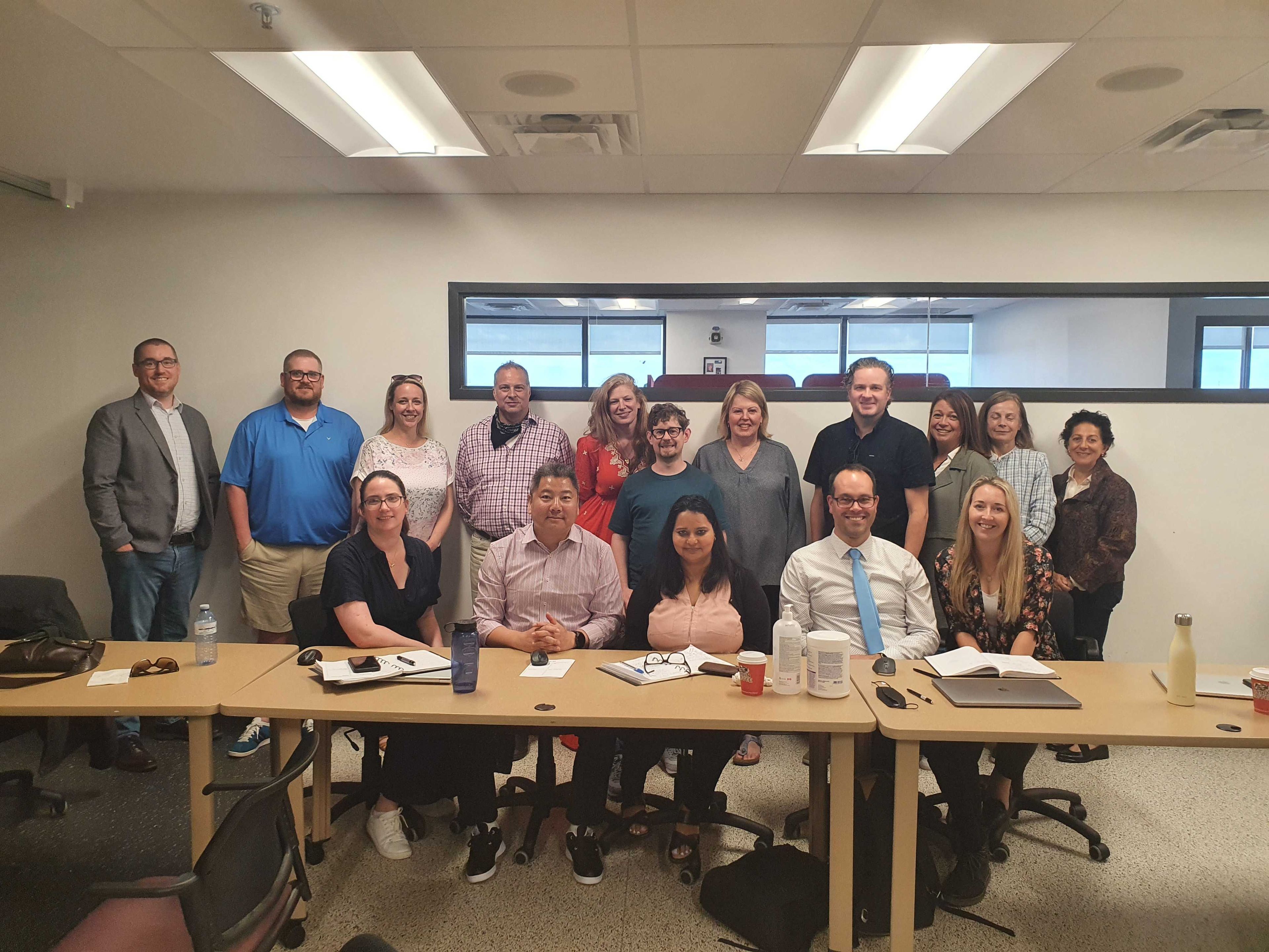 A dozen of people pose for camara in a group photo, behind a big desk in a room