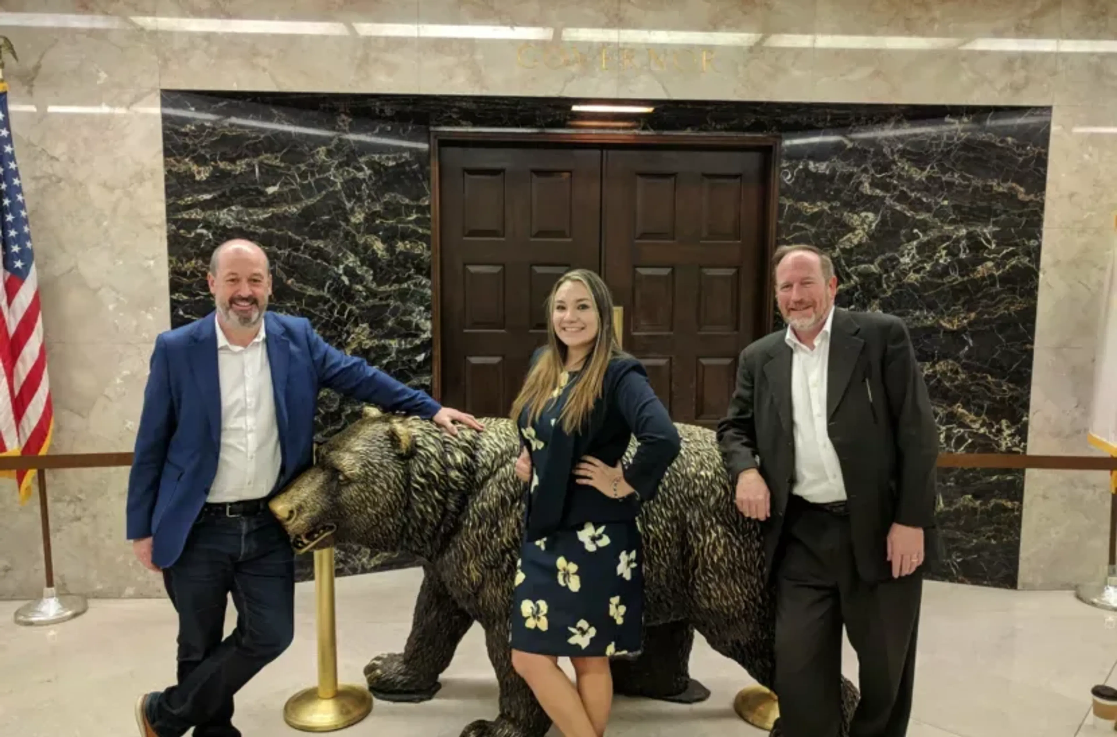 Three people in front of a California grizzly bear statue