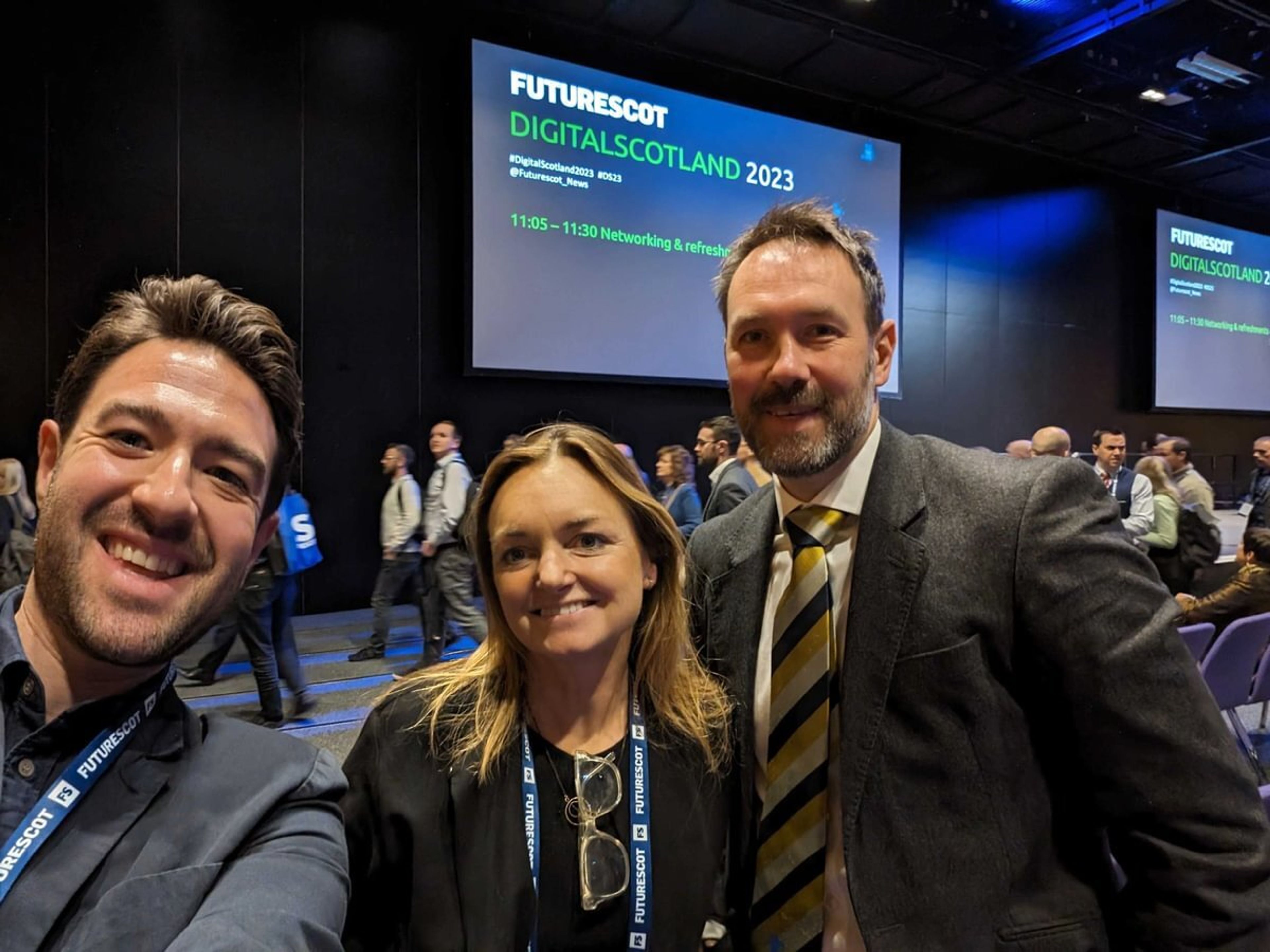 Three people posing for a selfie at a conference with a big screen behind them that reads "Digital Scotland 2023"