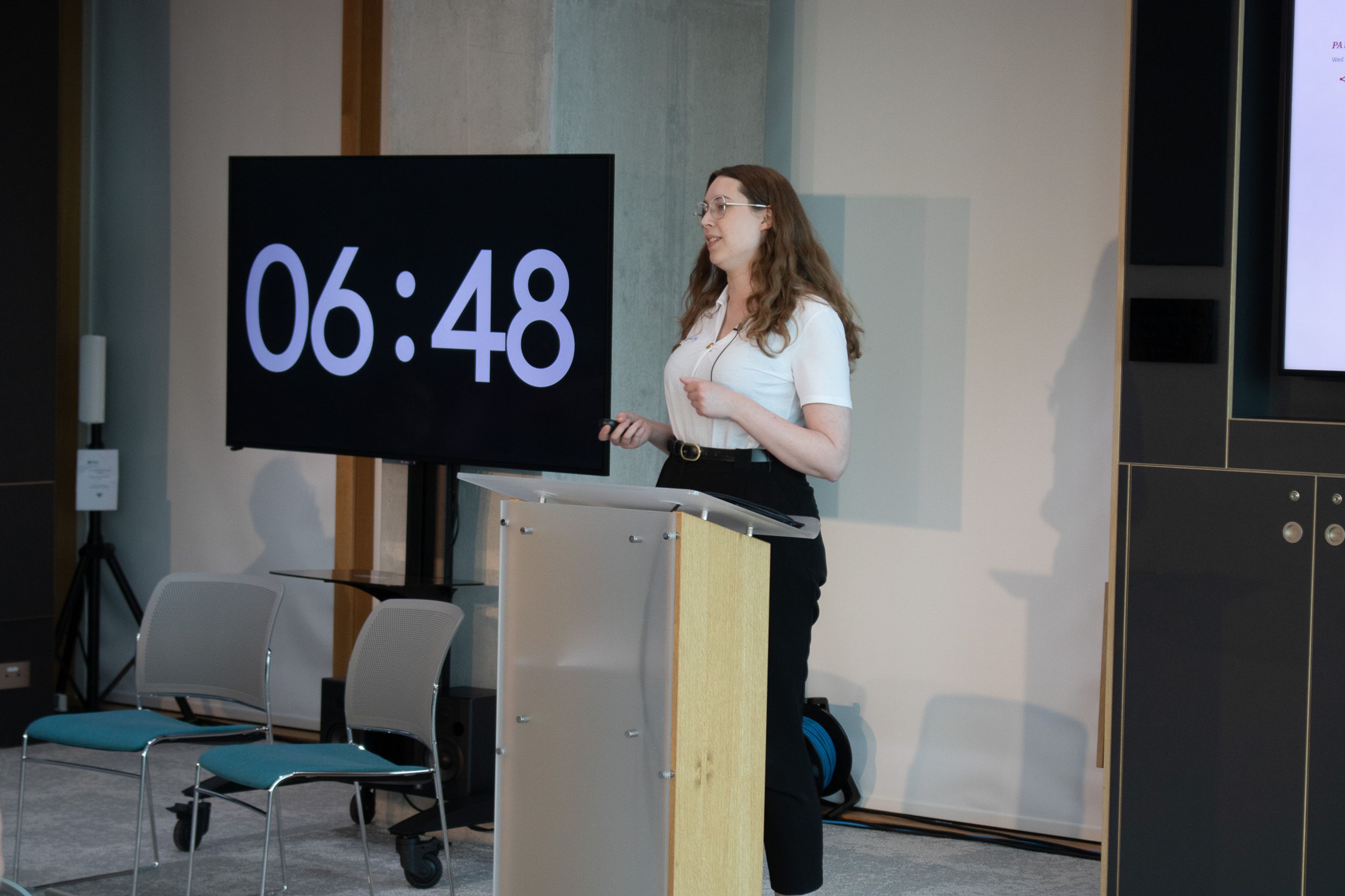 A woman addresses an audience with a screen counting time down behind her
