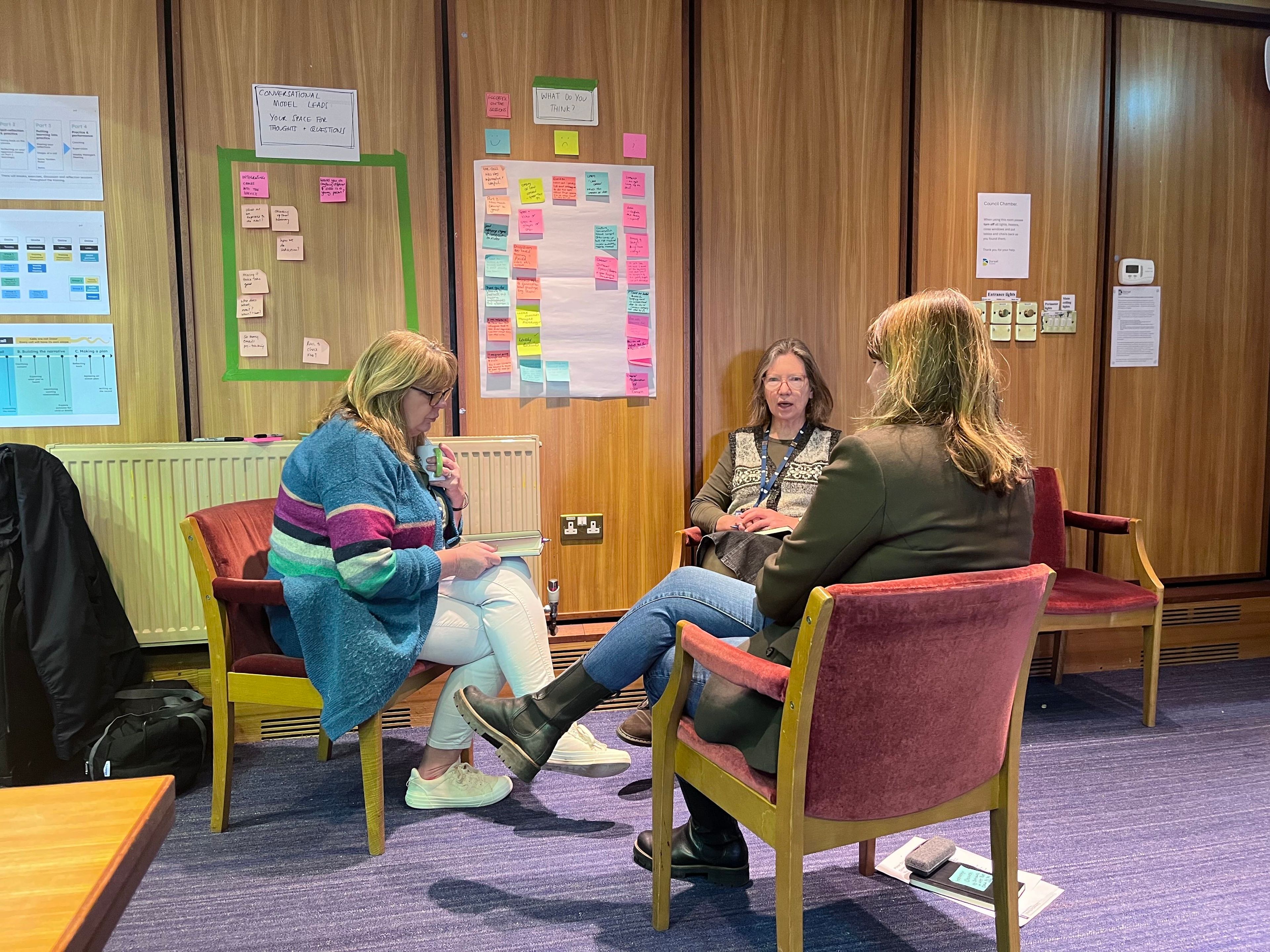 Three people sat in chairs surrounded by walls with paper artifacts