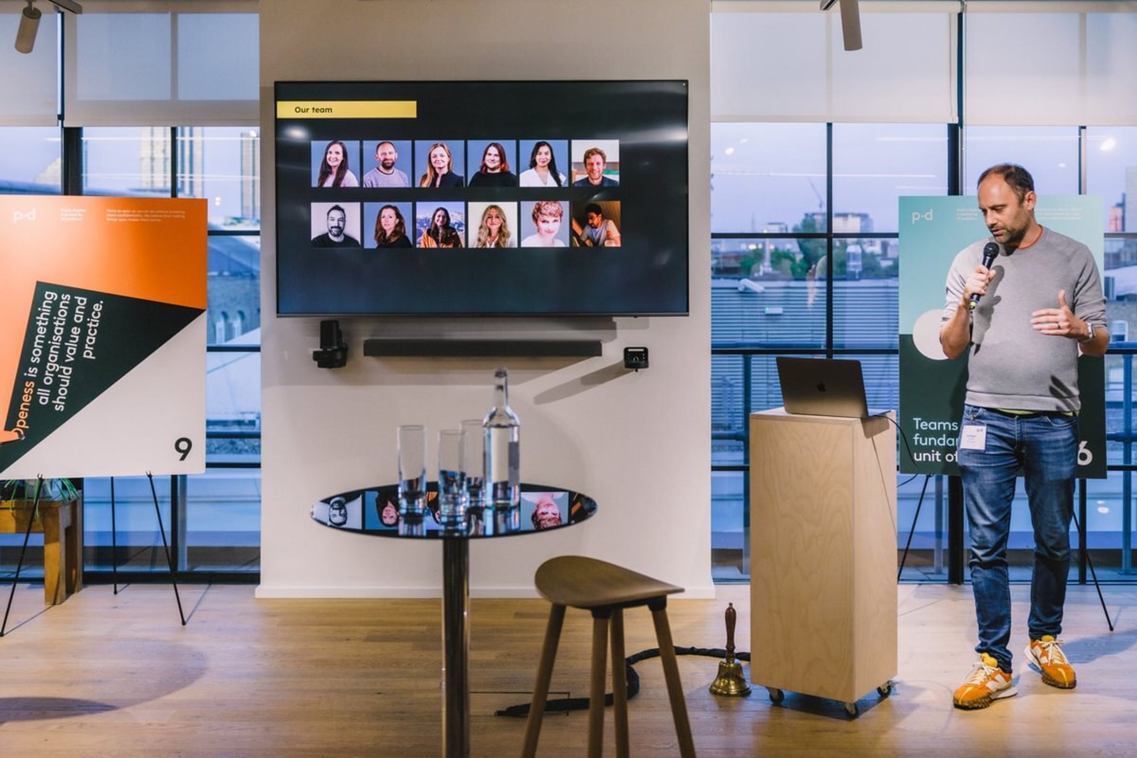 A presenter addresses an audience next to a screen that reads "our team" and a gallery of thumbnails