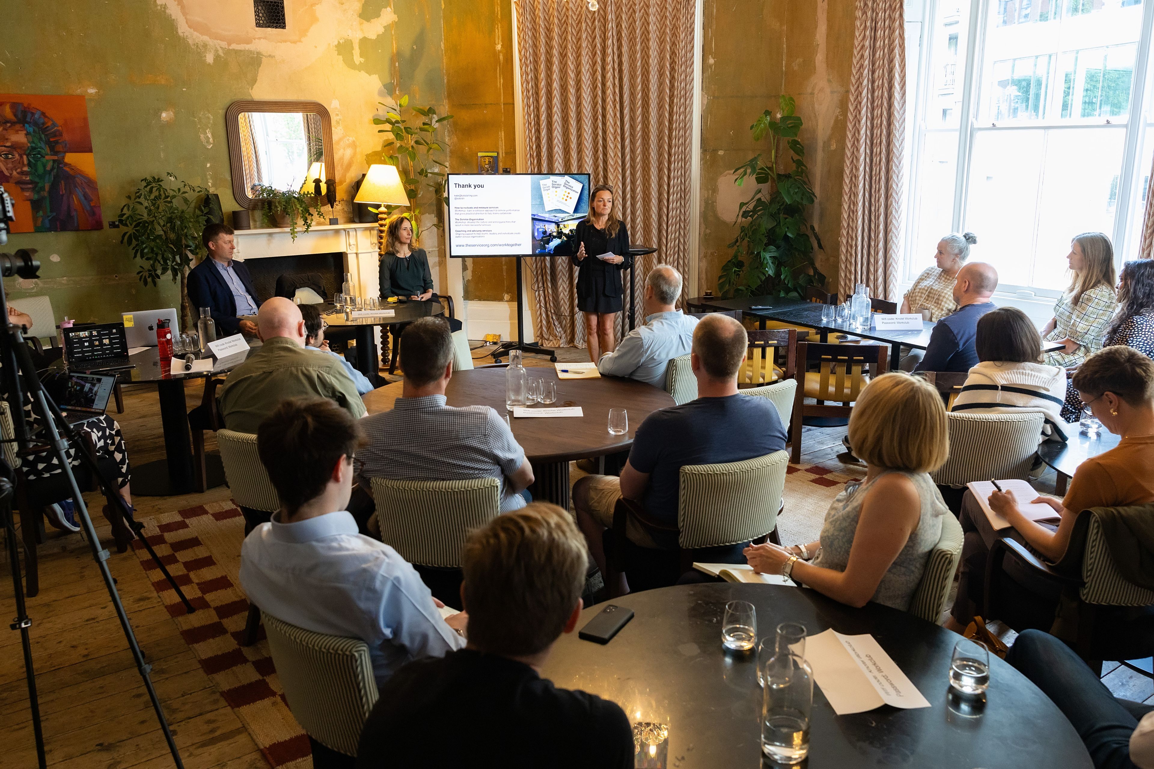 A presenter next to a screen engages a small room of professionals in attendance