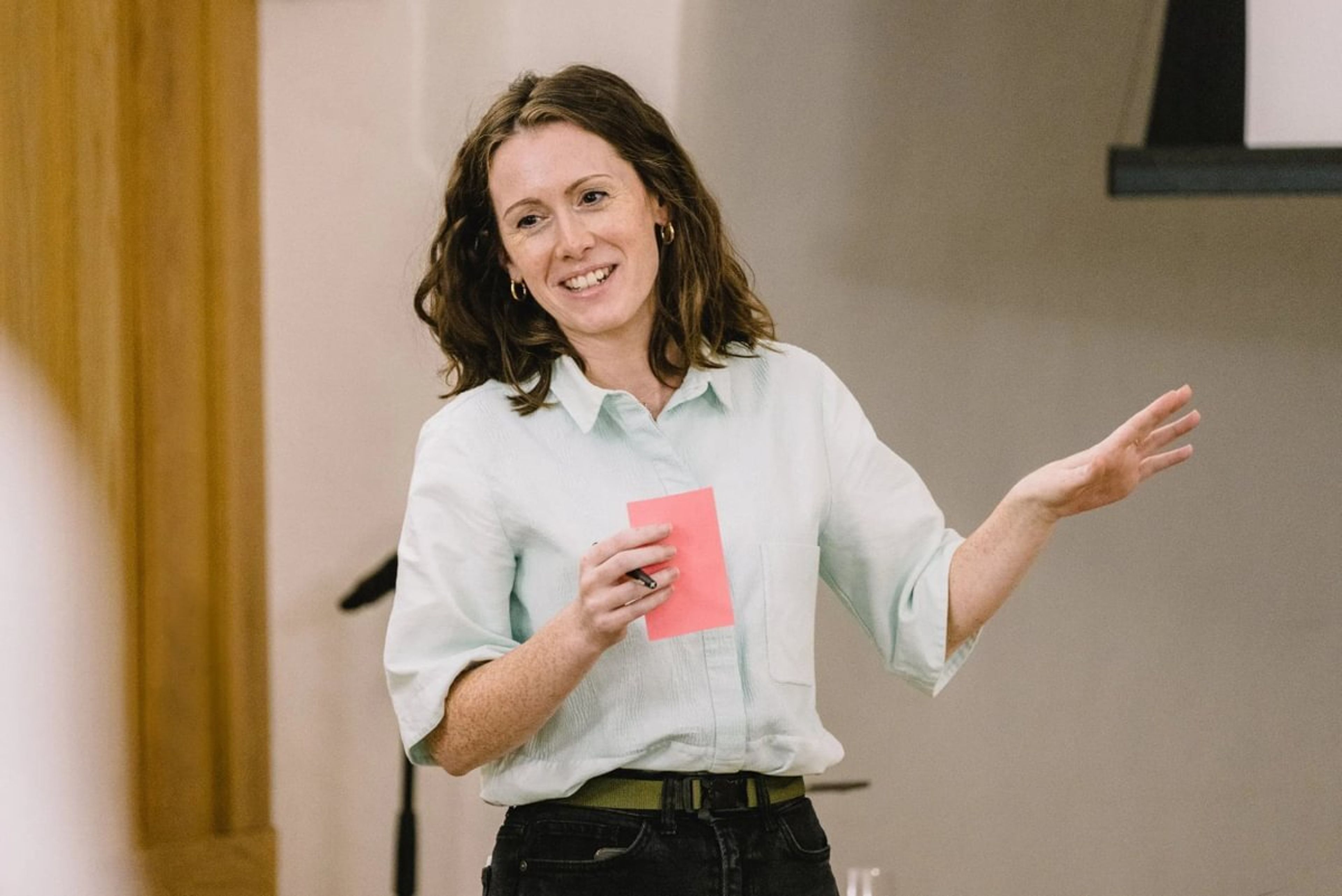 A female consultant is speaking in public while smiling and holding a pink card