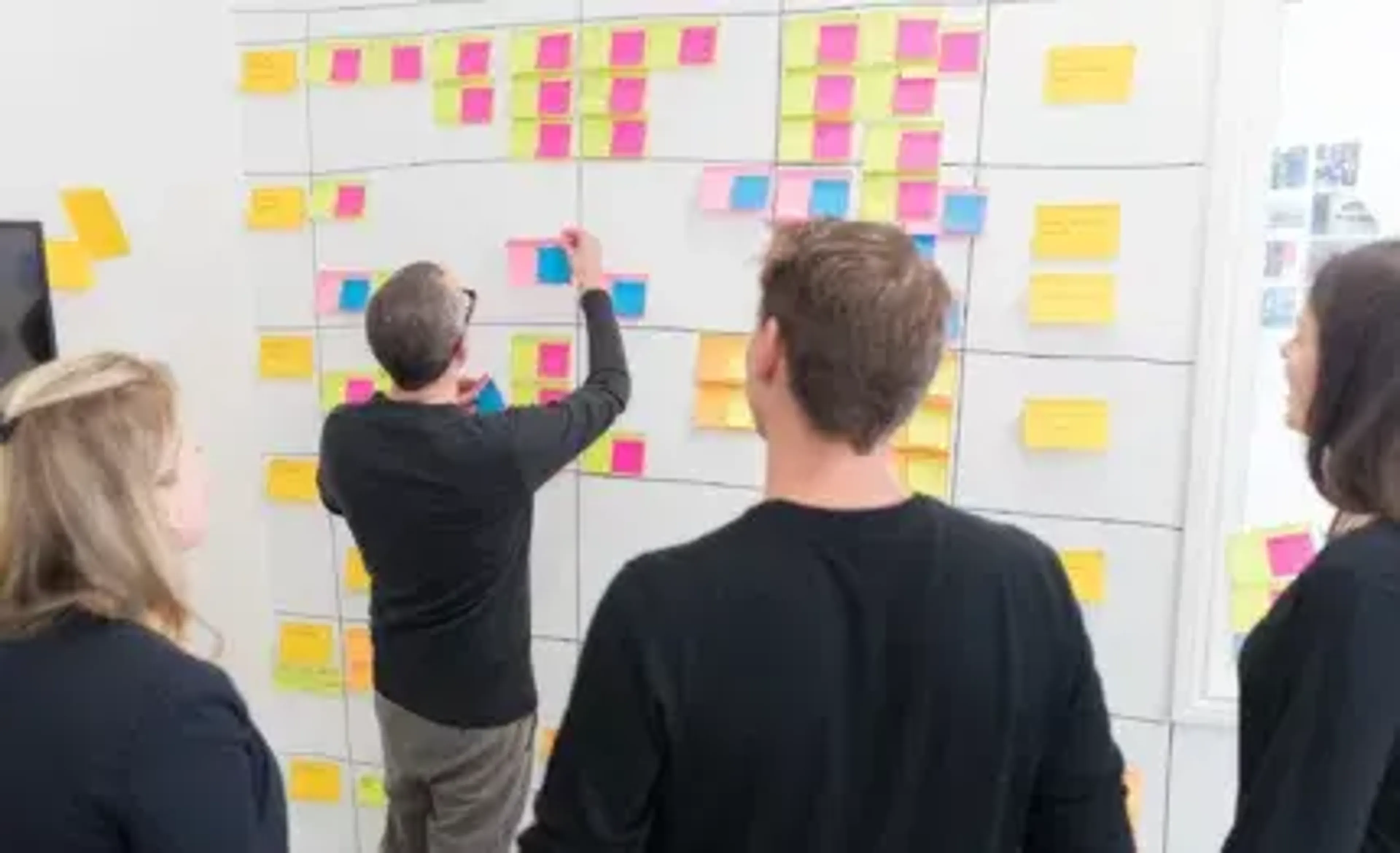 A man is putting posters on a wall with a team behind him