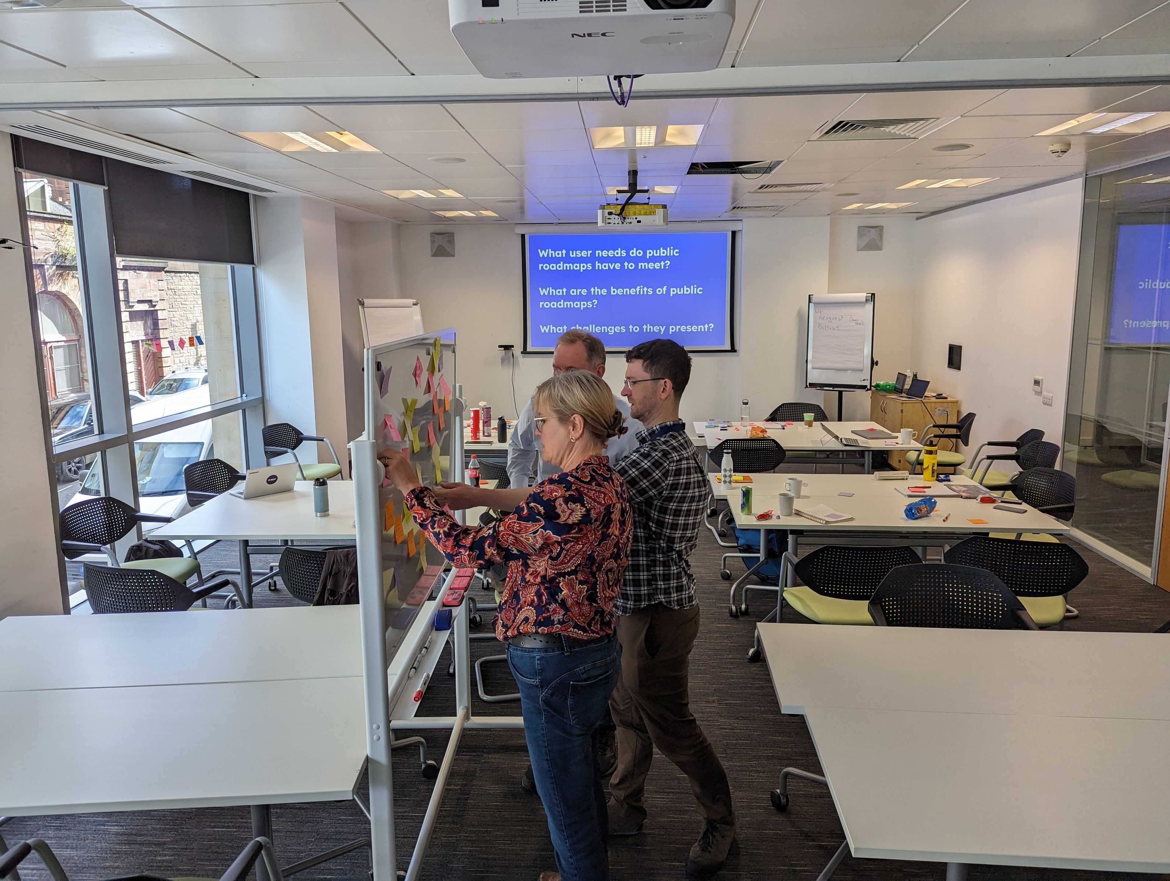 Three people working together on a room with a screen at the back asking questions about the challenges and benefits of working in the open