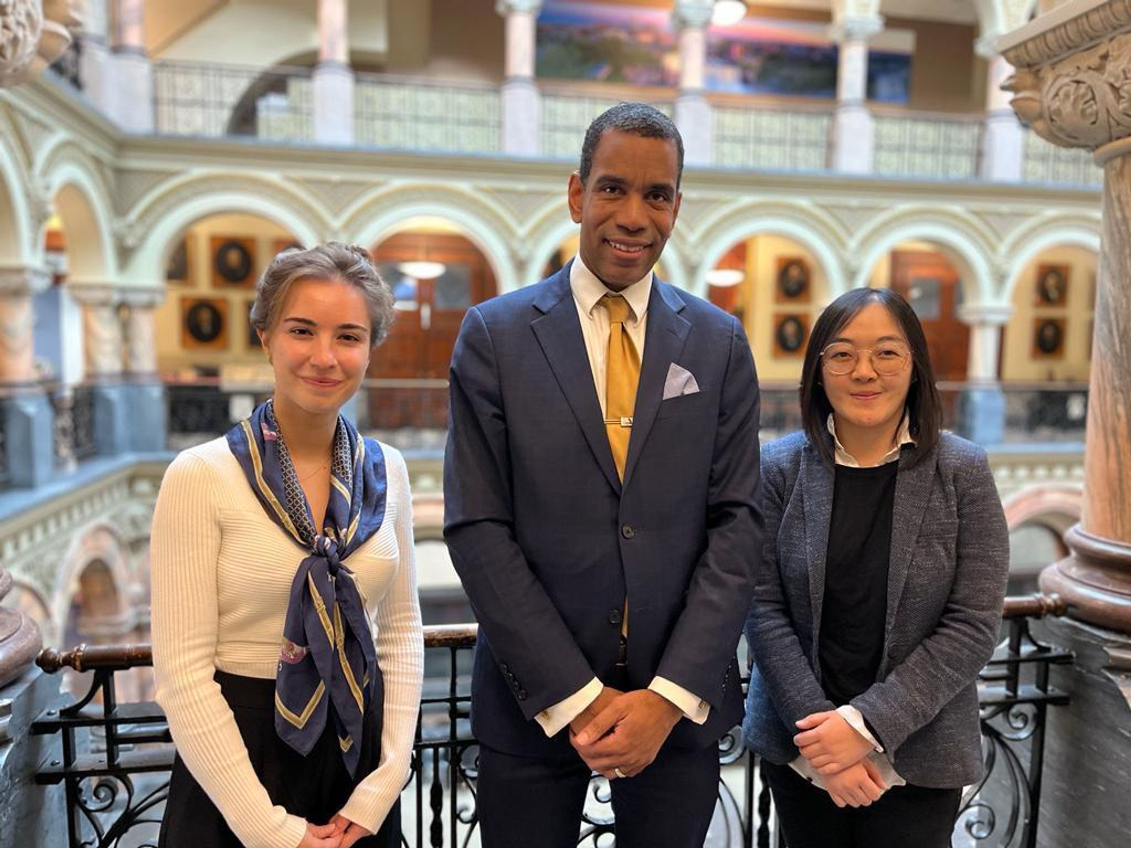 Two women and a man pose to camera in a balcony inside Rochester City Hall