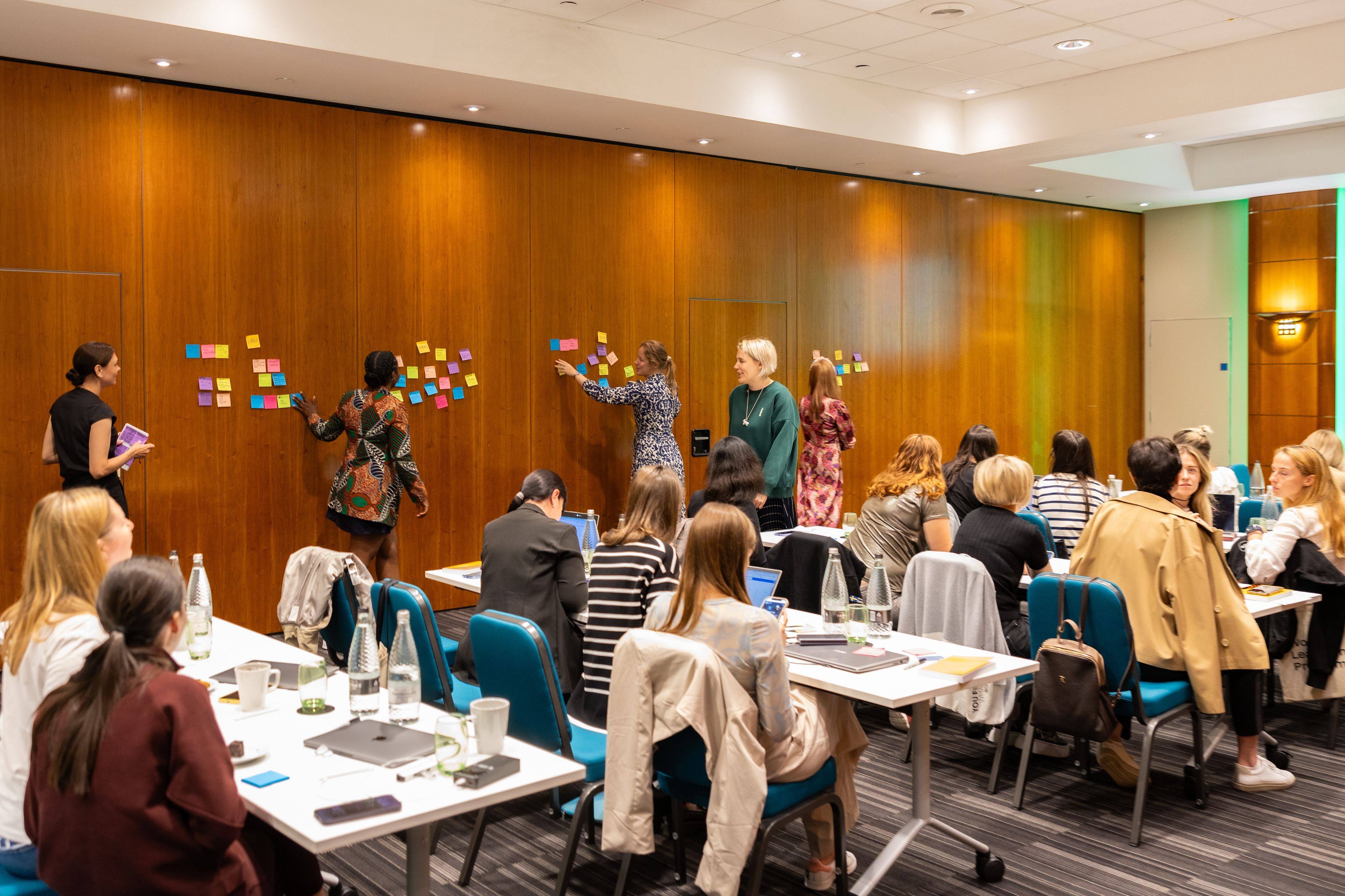 Four people working with post-its on a wall as part of a bigger workshop with over a dozen delegates