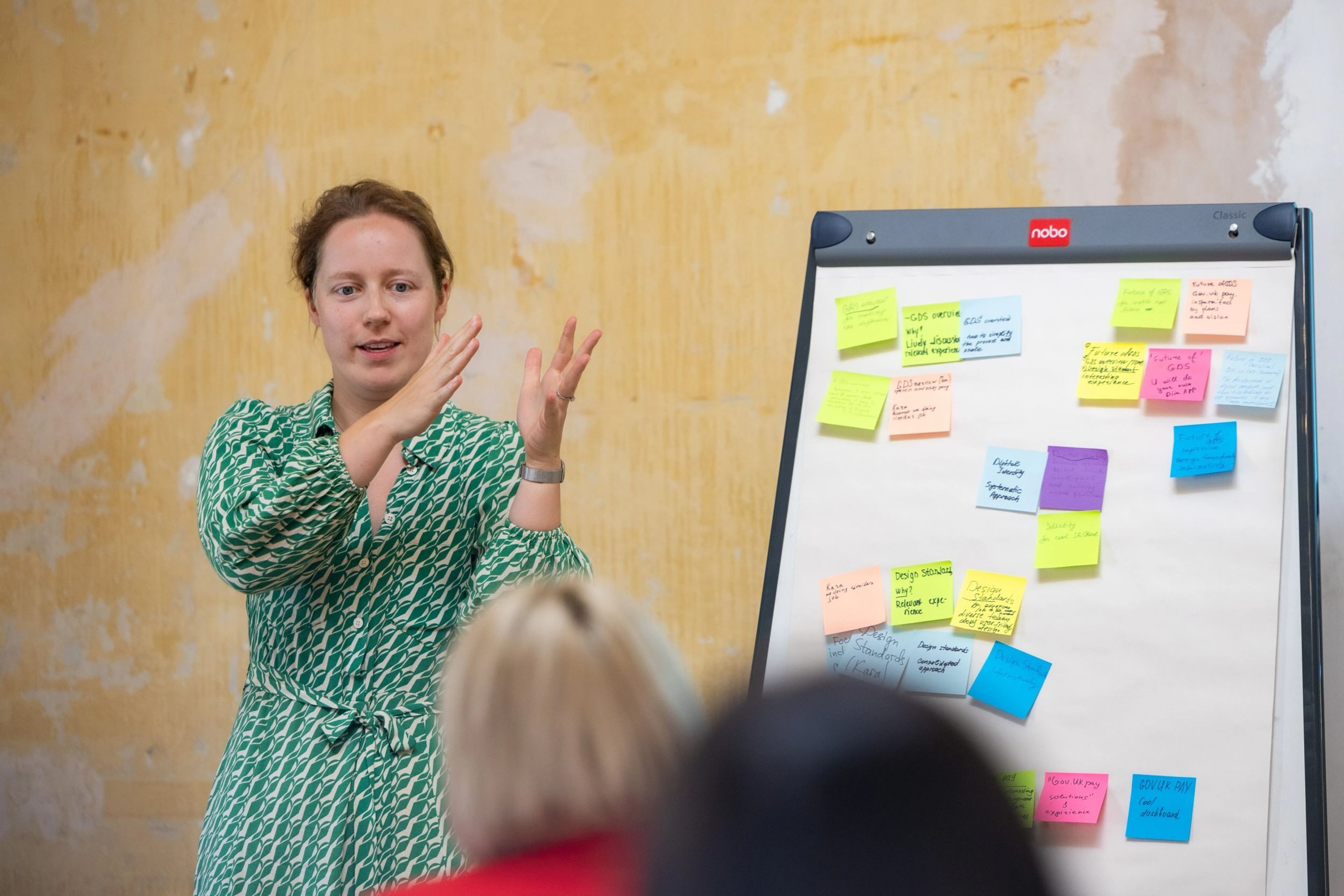 A woman doing a presentation next to a flipboard full of post-it notes