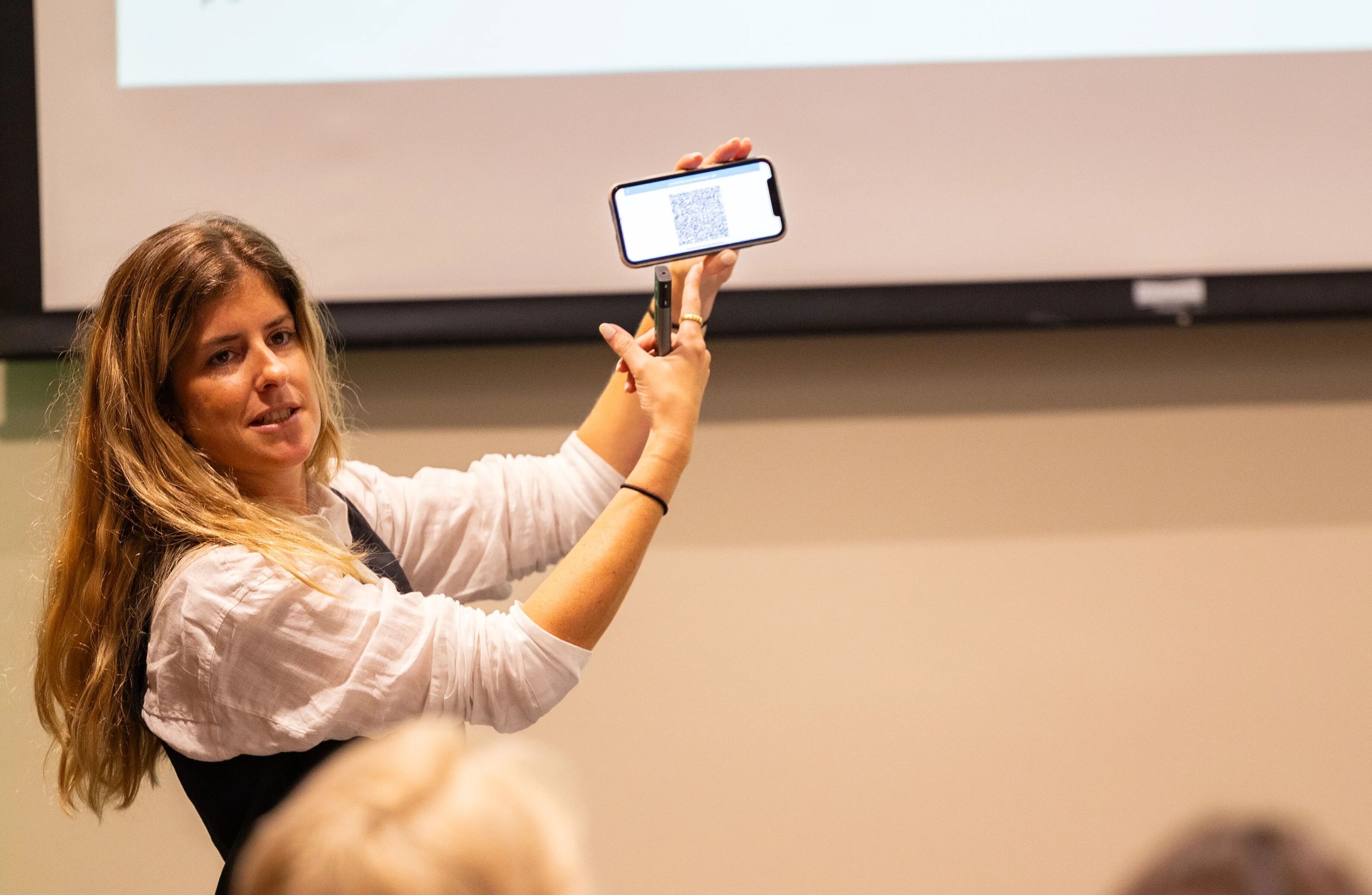 A woman shows a phone to an audience with a QR code in it