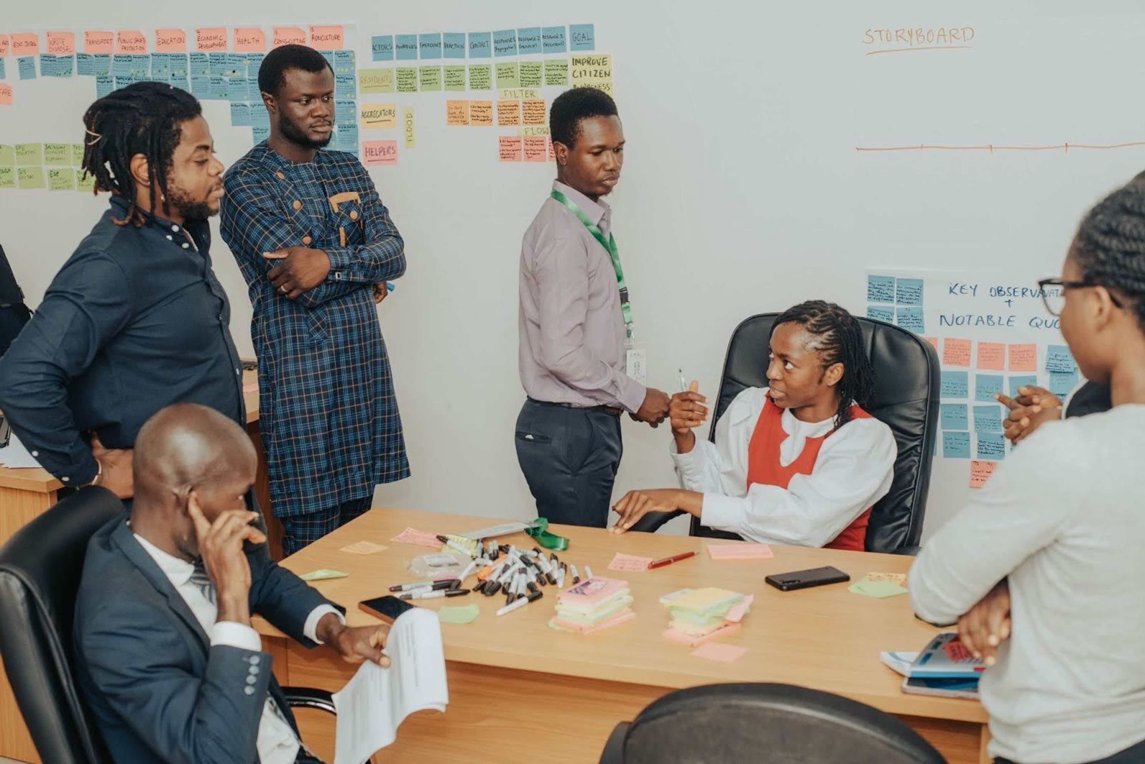 A group of participants sitting and standing around a table in a room full of workshop artifacts