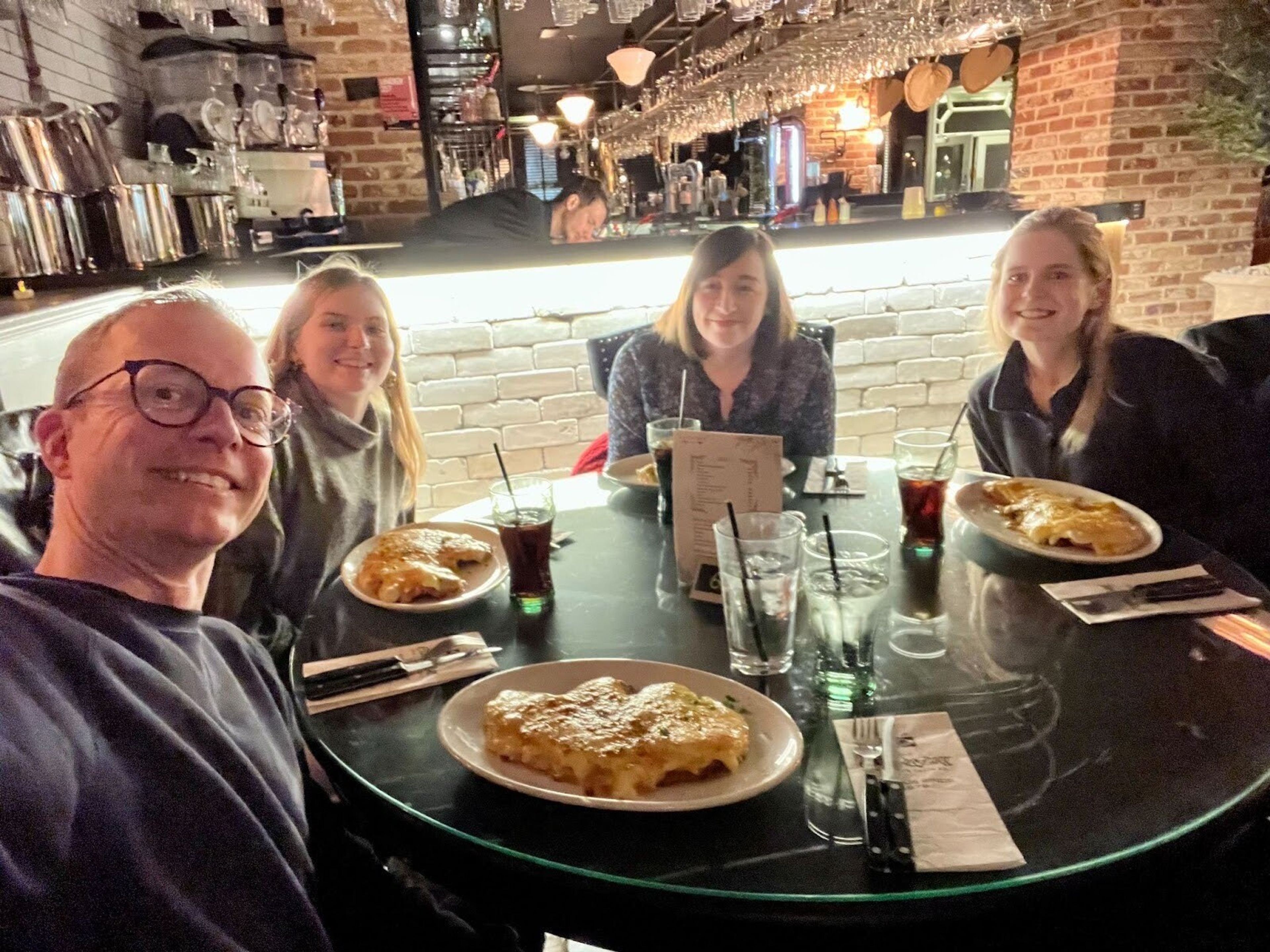 Four people sharing a meal take a selfie smiling to camera