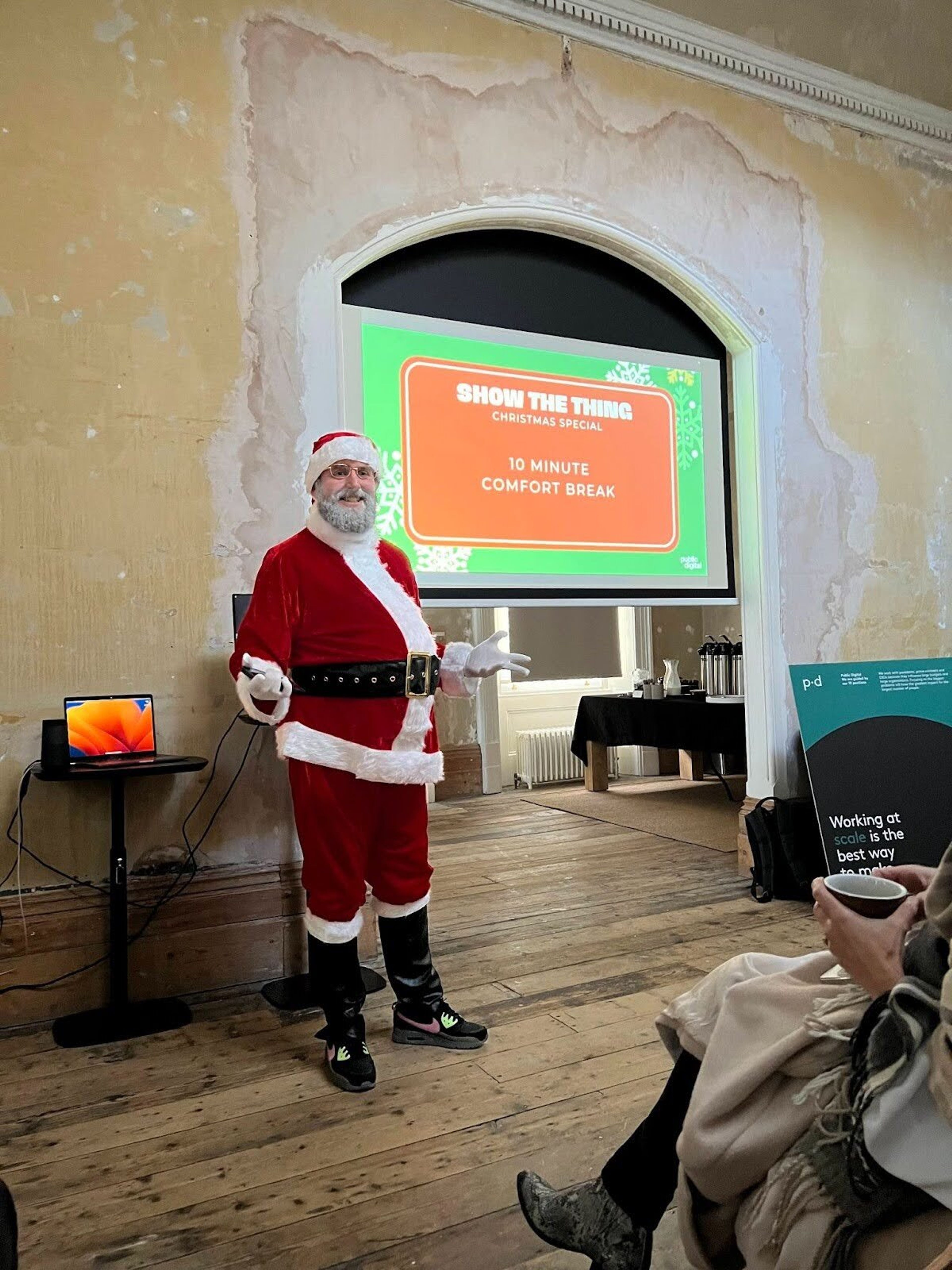 A man dressed up as Santa delivers a presentation with the words on screen "Show the thing"