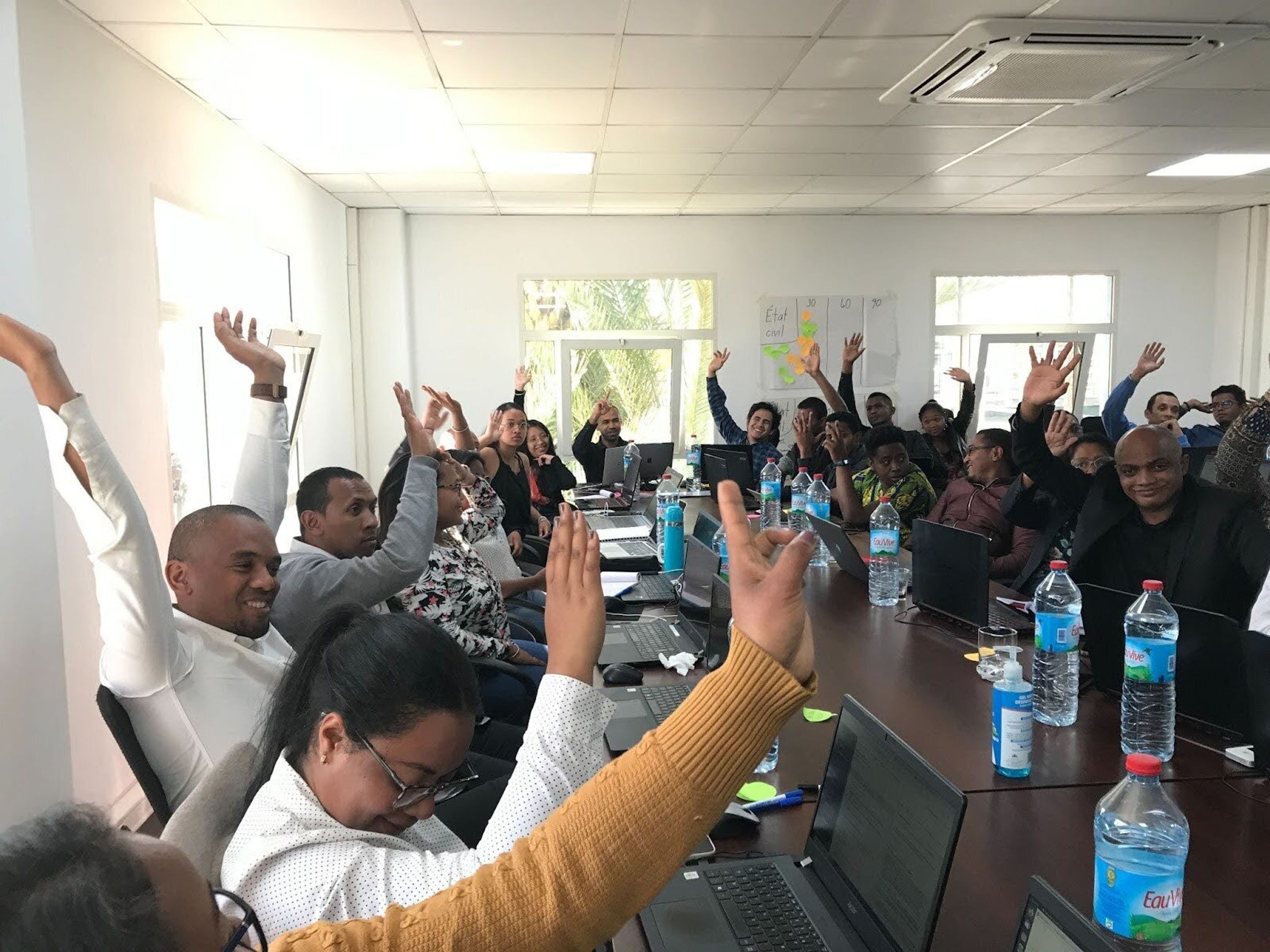 A group of participants in a workshop all raise their hands with amused faces