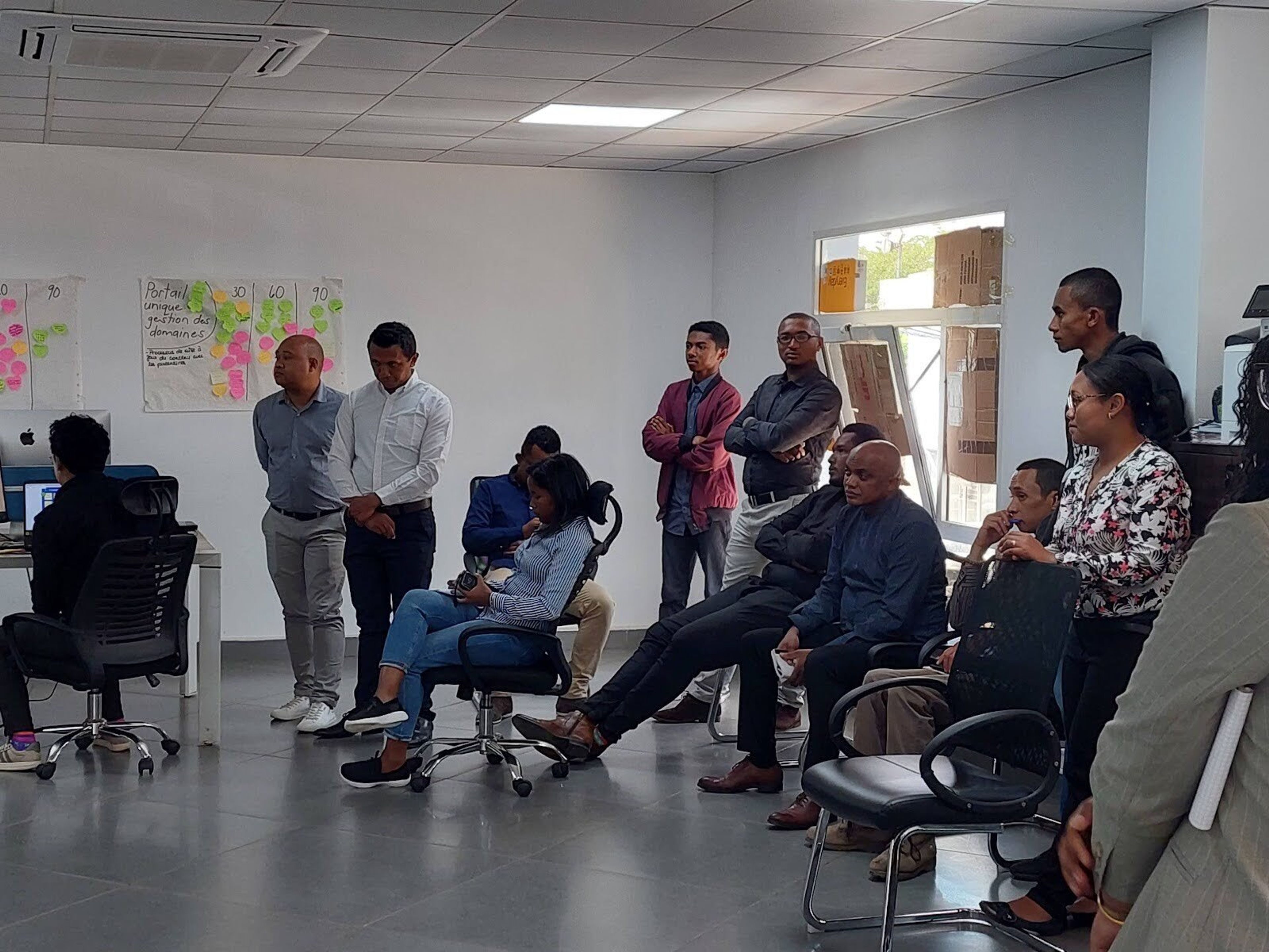 A group of professionals sit and stand casually paying attention to a presenter