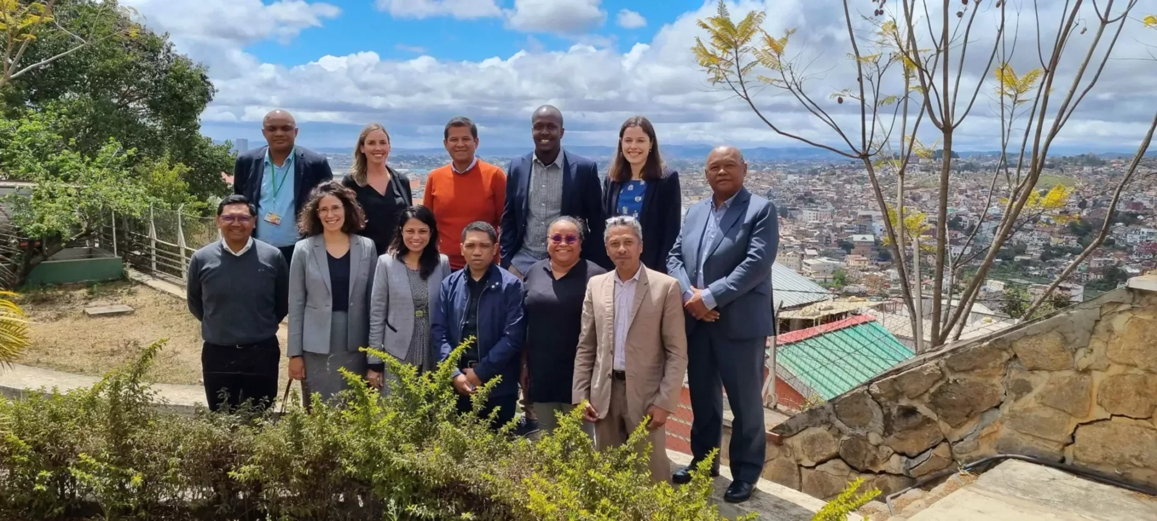 A delegation of 12 people stand in a sunny day outside for a group picture