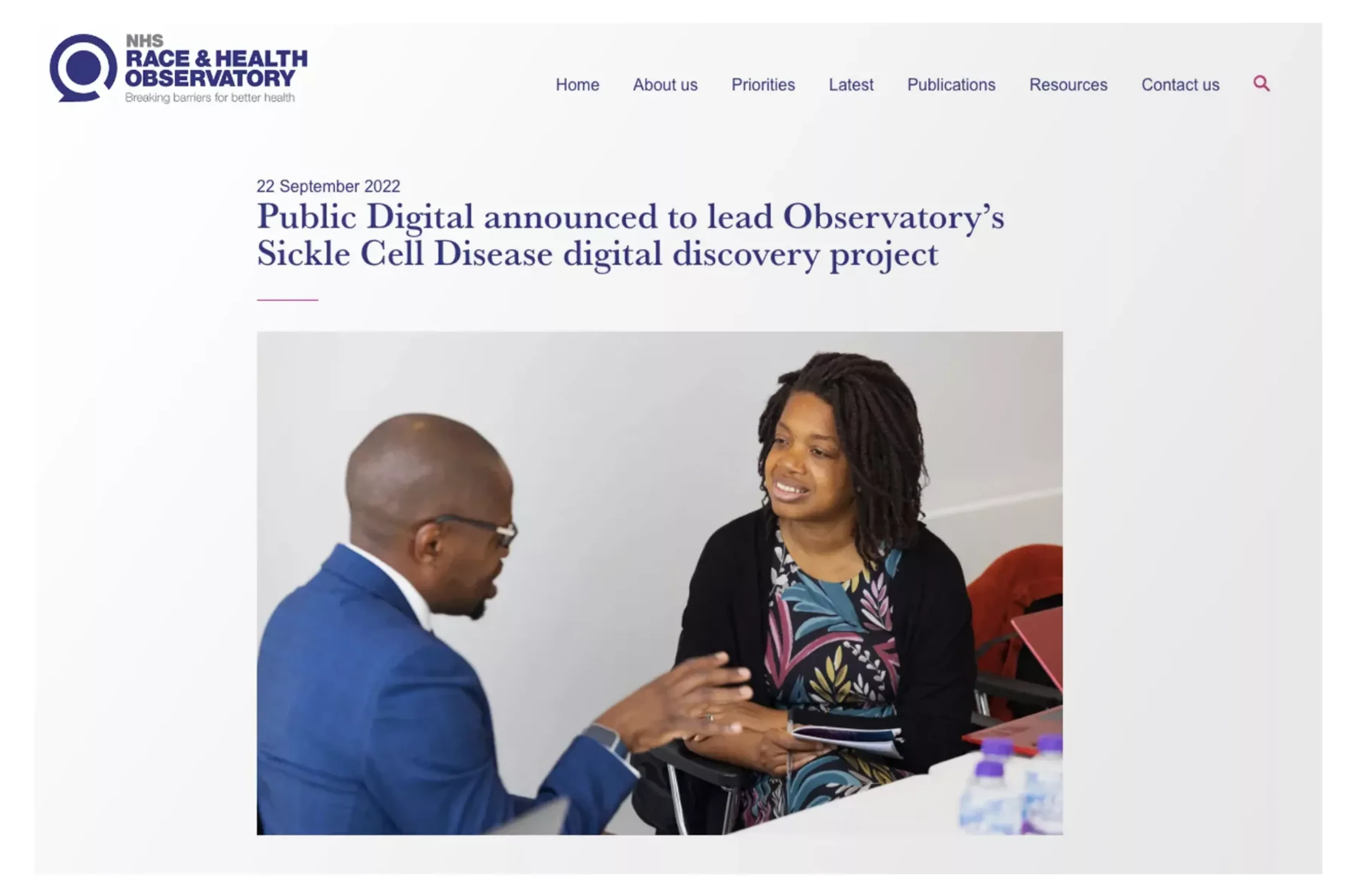 A screenshot of the NHS Race and Health Observatory's article. The article is called: "Public Digital announced to lead Observatory’s Sickle Cell Disease digital discovery project" and it has a photograph of two people speaking to each other, taken at our launch event at the Sickle Cell Society offices earlier this month.